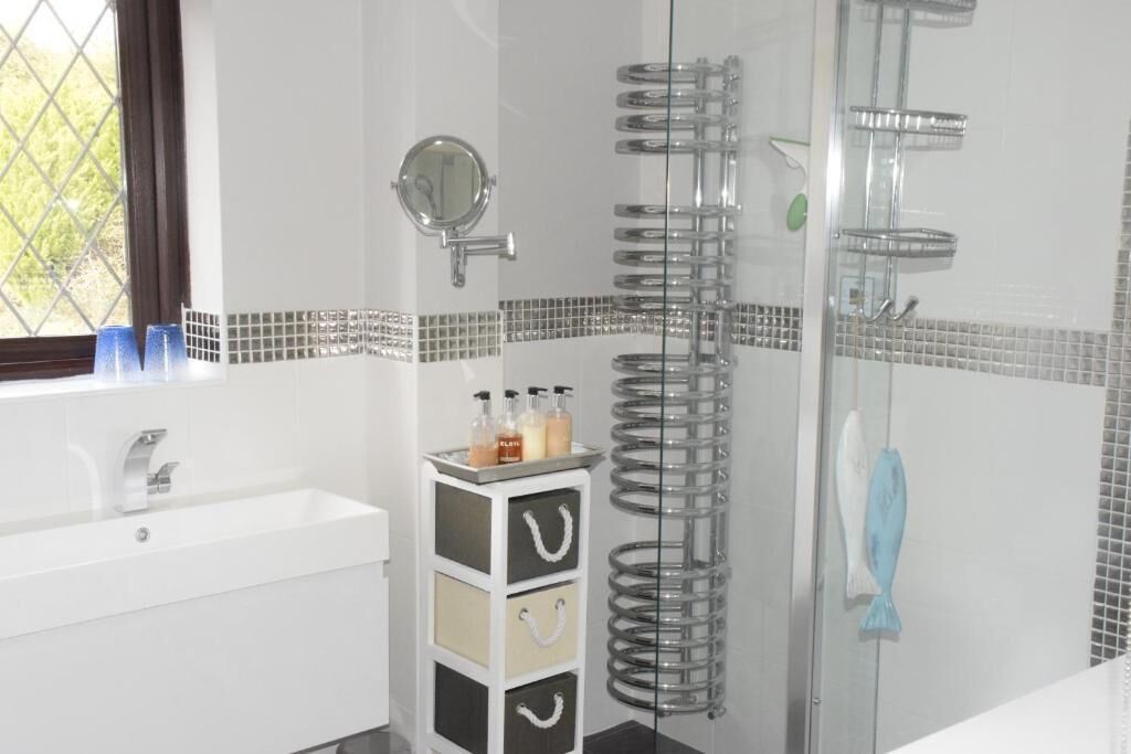 Un baño con un lavamanos blanco, un espejo, una ducha con puerta de vidrio y una ventana con vistas.