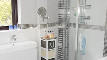 Un baño con un lavamanos blanco, un espejo, una ducha con puerta de vidrio y una ventana con vistas.