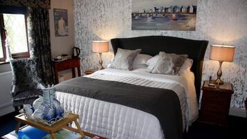 Ett hotellrum med en stor säng, två sängbord med lampor, en stol, ett fönster med gardiner och en tavla på väggen.