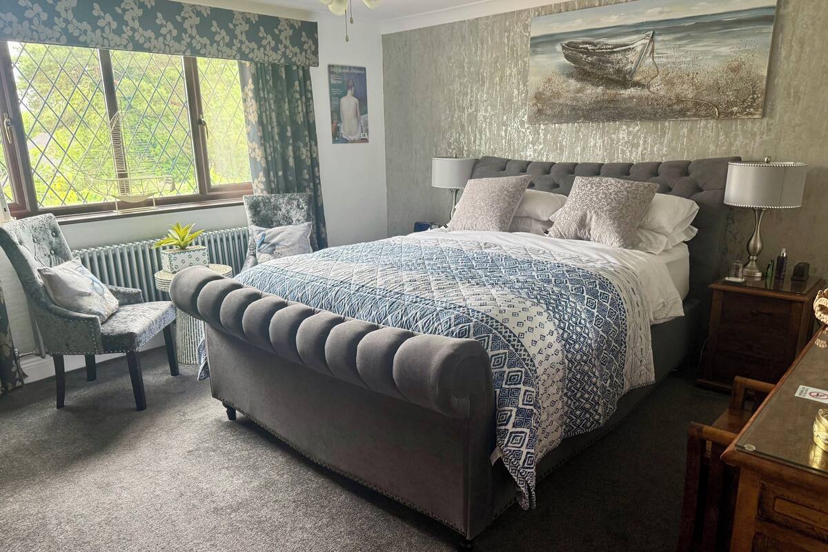 Un dormitorio con una cama grande, una silla, un escritorio y una ventana con cortinas.