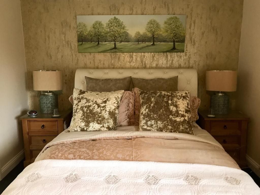 A bedroom with a bed, two bedside tables, lamps, a painting on the wall, and a patterned bedspread.