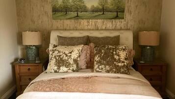 A bedroom with a bed, two bedside tables, lamps, a painting on the wall, and a patterned bedspread.