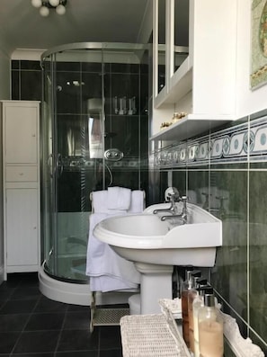 Une salle de bain avec une douche à parois de verre, un lavabo blanc et un mur recouvert de carreaux.