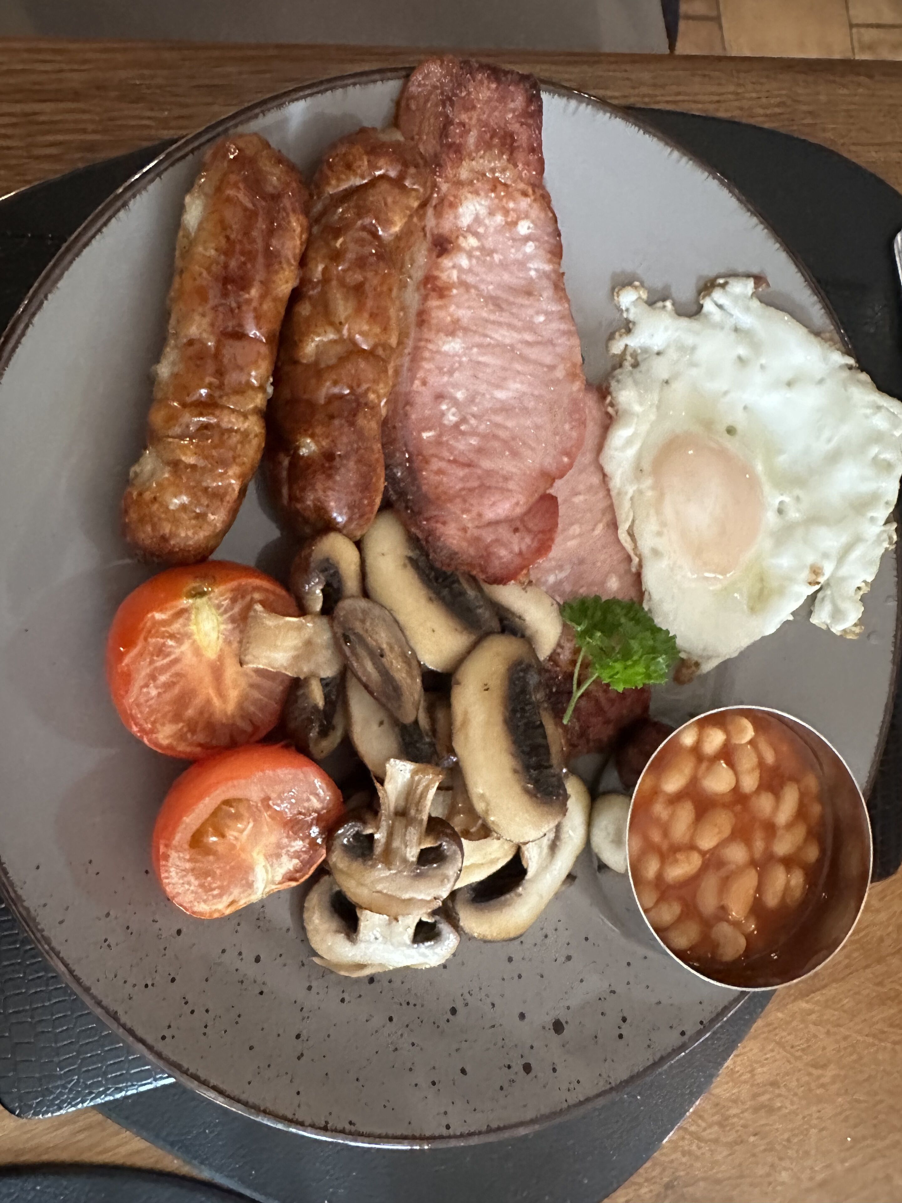 Un plato de comida para el desayuno con salchichas, un huevo frito, champiñones, tomates y frijoles horneados.
