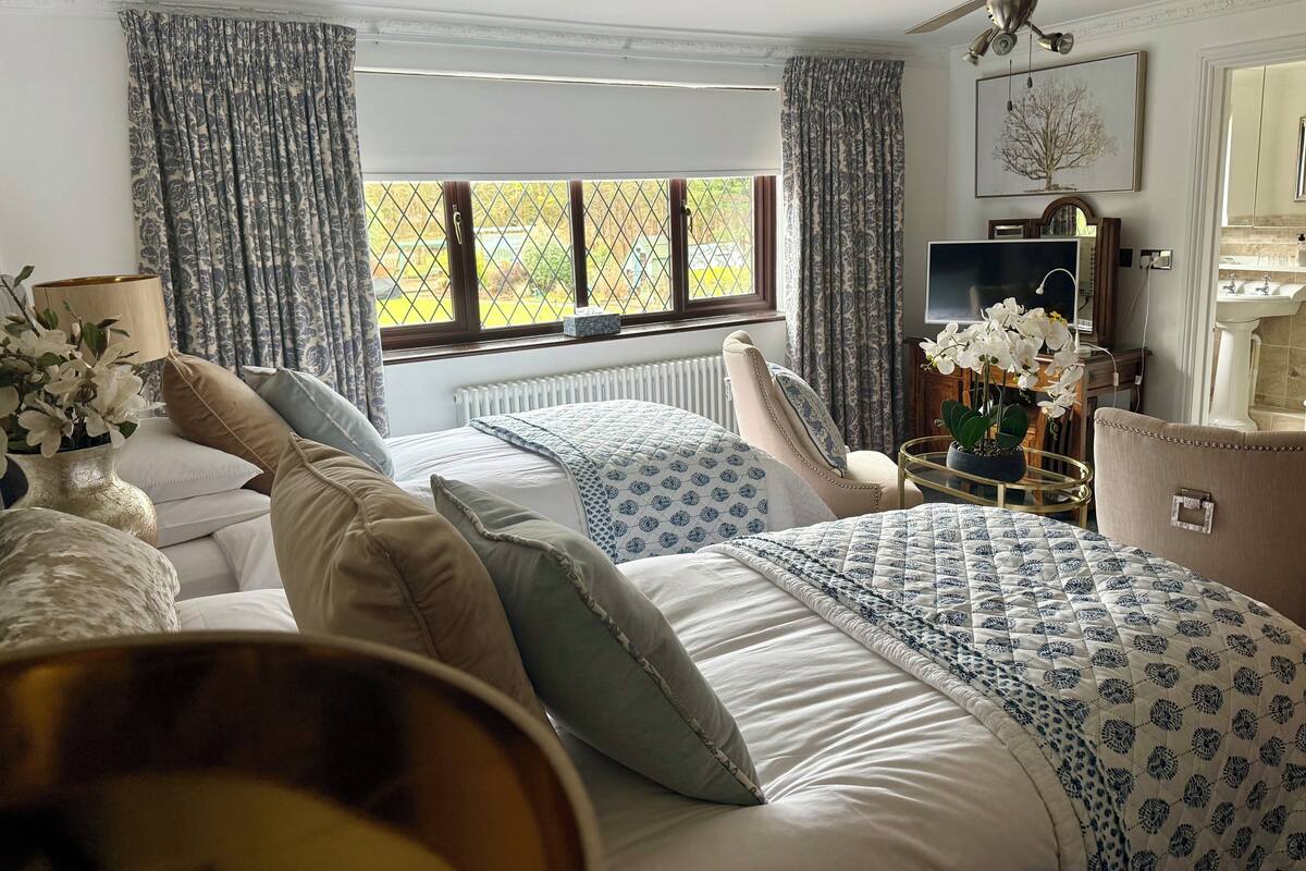 Un dormitorio con una cama grande, ventilador de techo, ventana con cortinas, radiador, televisor y lavamanos.