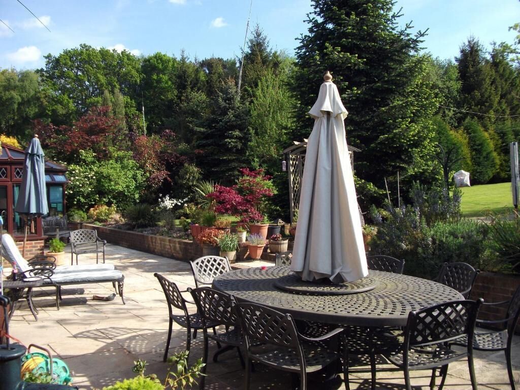 An outdoor patio with a round table and chairs, surrounded by potted plants and a lawn.