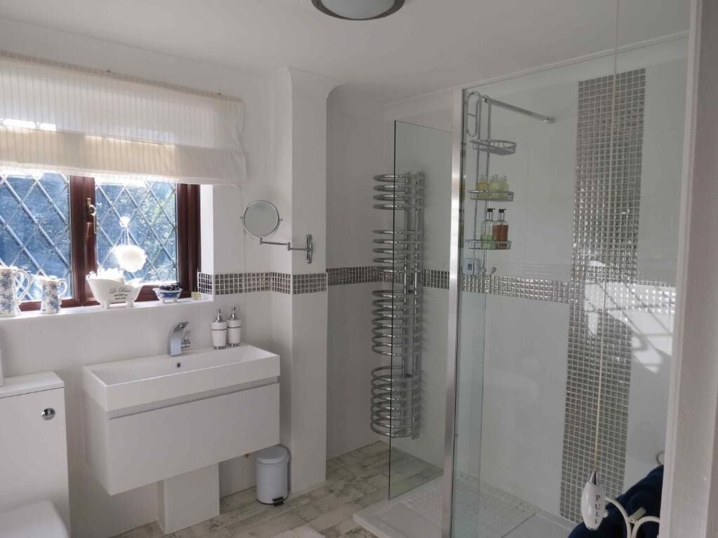 Un baño con cabina de ducha de vidrio, un lavamanos blanco y una ventana con cortinas.