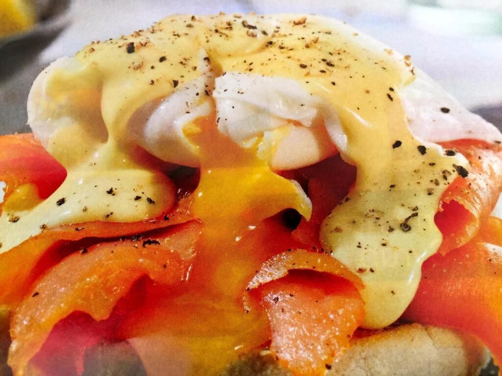 A close-up of a dish with poached eggs, smoked salmon, and hollandaise sauce.