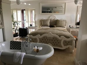 A bedroom with a large bed, a bathtub, and a mirror above the bed. - Beechwood B&B (Lewes)
