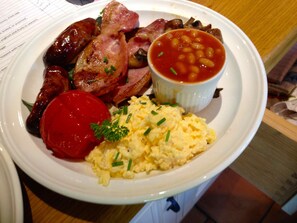 Un plato con huevos revueltos, salchichas, tocino, frijoles horneados y tomate.