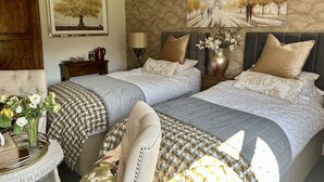 Un dormitorio con dos camas, una mesita de noche, una lámpara, un jarrón con flores y un ventilador de techo.