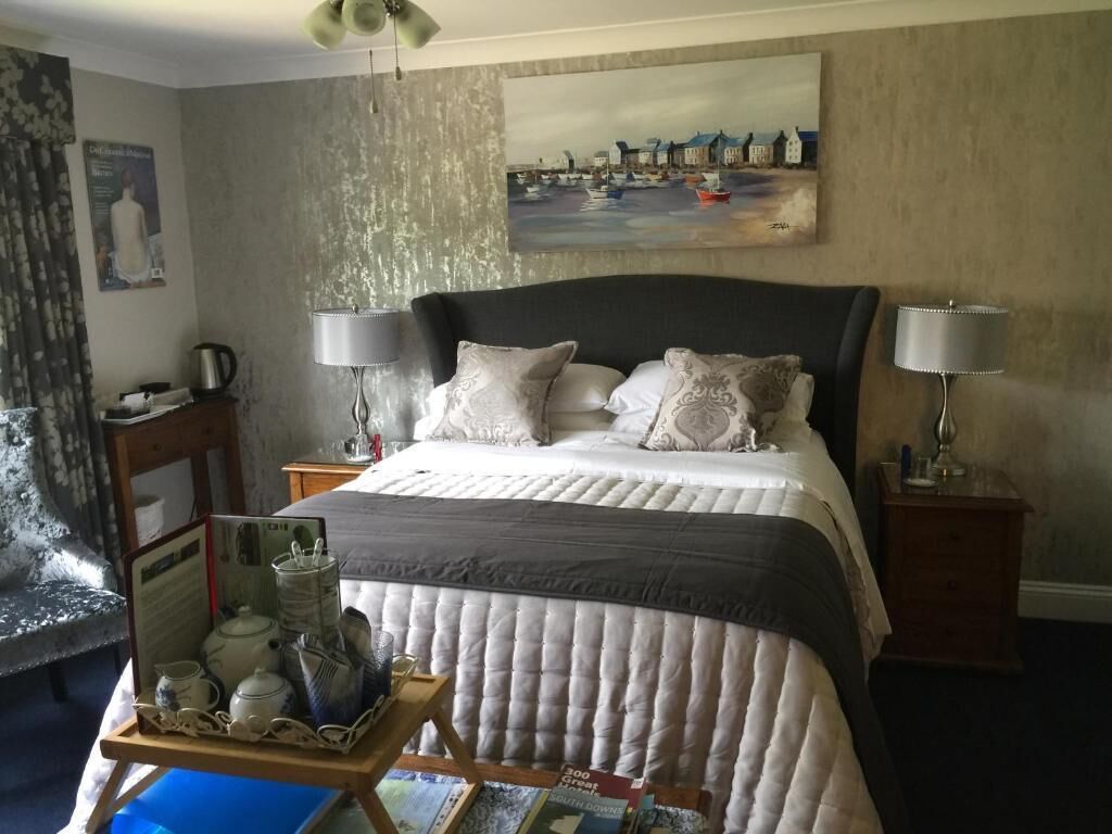 A bedroom with a large bed, two bedside tables with lamps, a painting on the wall, and a small table with decorative items.