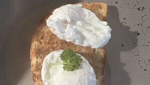 Una rebanada de tostada con dos cucharadas de crema blanca y una ramita de perejil sobre un plato.