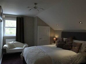 A bedroom with a bed, a chair, a ceiling fan, and a window with curtains. - Causeway Lodge (Bushmills)