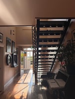 Un interior moderno con una escalera, una zona de estar con una mesa y una puerta que da al exterior.