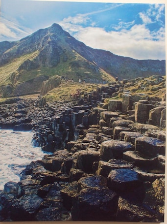 A rugged coastal landscape with large boulders and a mountain in the background.