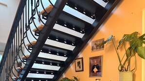 A staircase with a black metal railing, a green chair, a wooden side table with a plant, and a desk with a guitar. - Causeway Lodge (Bushmills)
