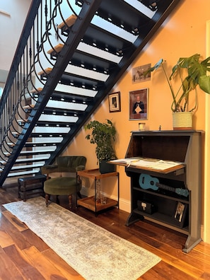 A staircase with a black metal railing, a green chair, a wooden side table with a plant, and a desk with a guitar. - Causeway Lodge (Bushmills)