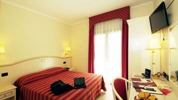 Habitación de hotel con una cama, un escritorio con una computadora portátil, un plato de comida y un televisor en la pared.