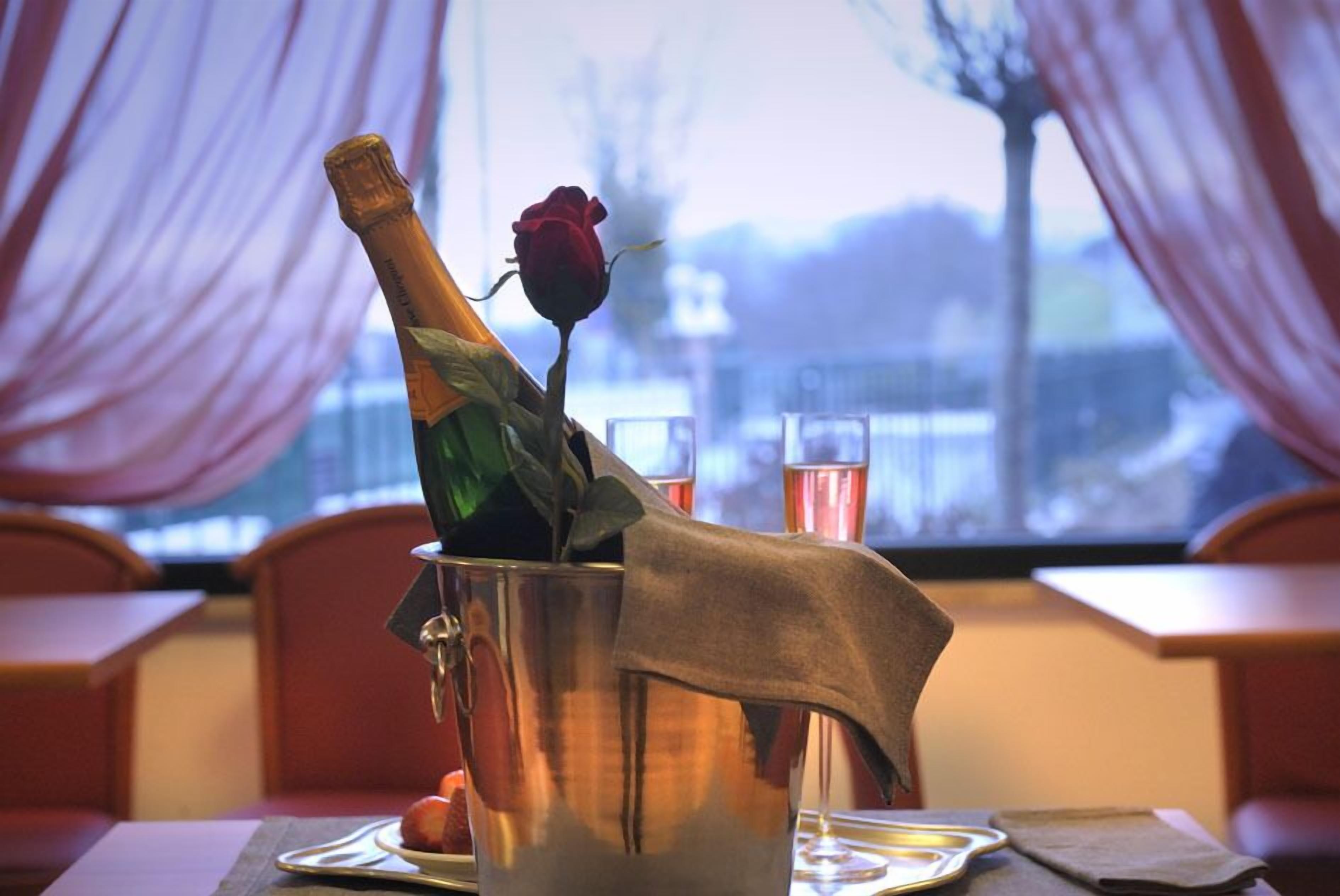 En flaska champagne i en silverhink, med en ros ovanpå, placerad på ett bord tillsammans med ett glas och en tallrik med frukt.