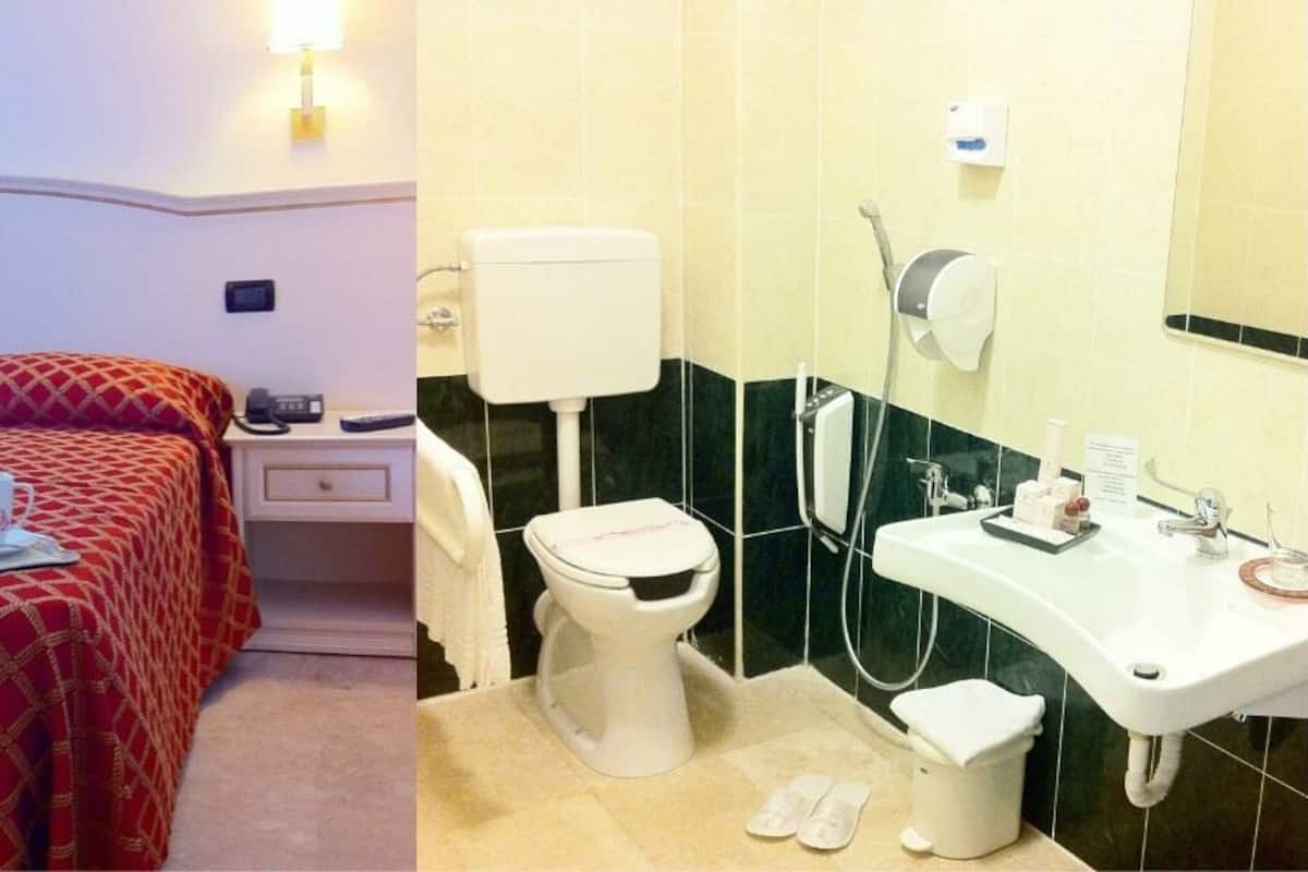 A hotel room with a bed, bedside table, and a bathroom with a toilet, sink, and shower.