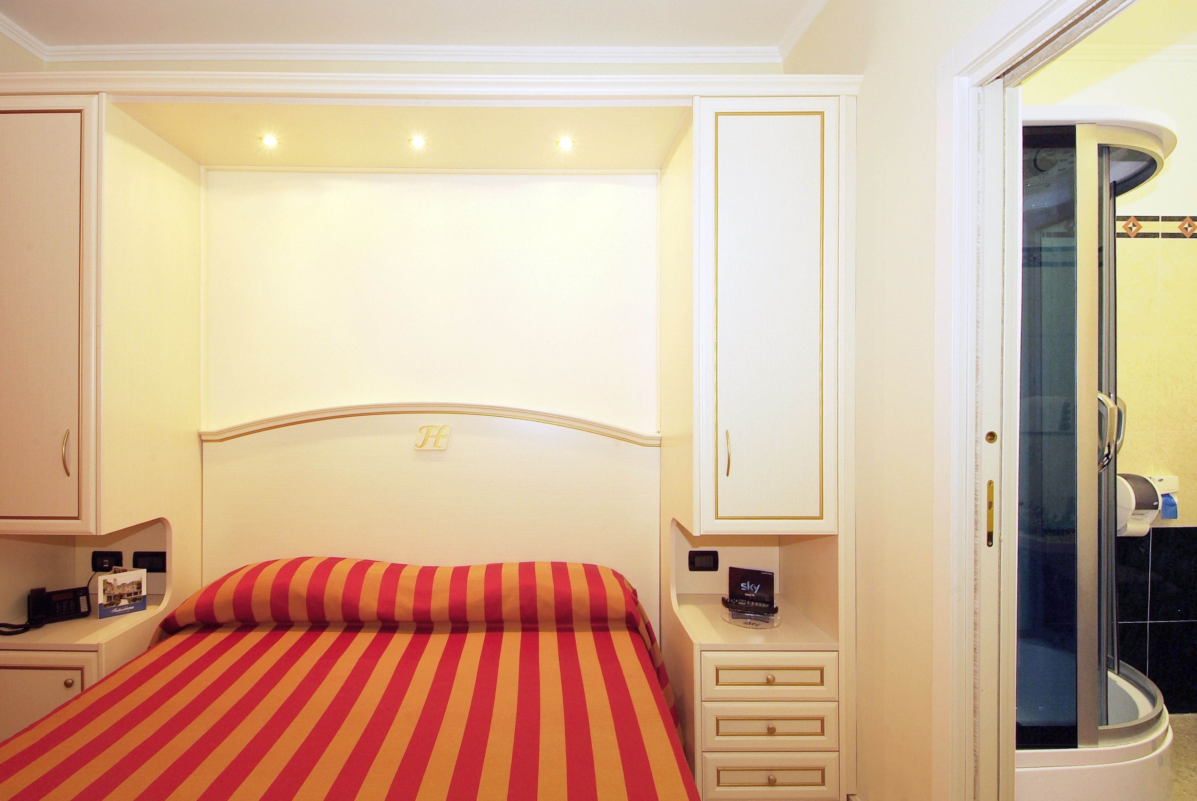 Habitación de hotel con cama, mesitas de noche, un espejo y zona de ducha.