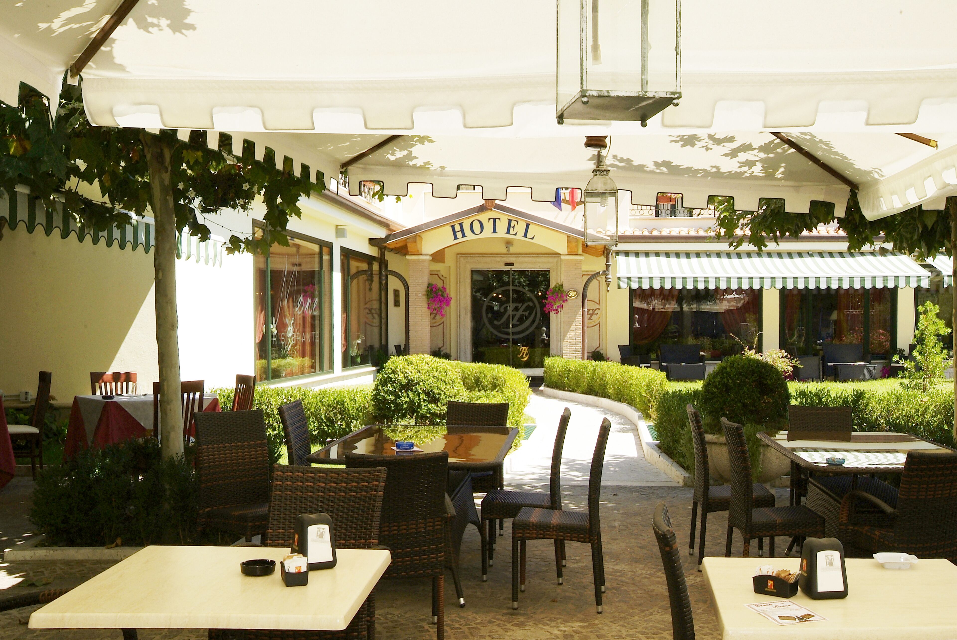 An outdoor seating area with wicker chairs and tables, a 'HOTEL' sign, and a well-maintained garden.
