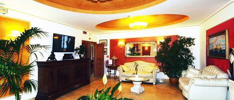 A spacious lobby with a large chandelier, a television, a sofa, and potted plants.