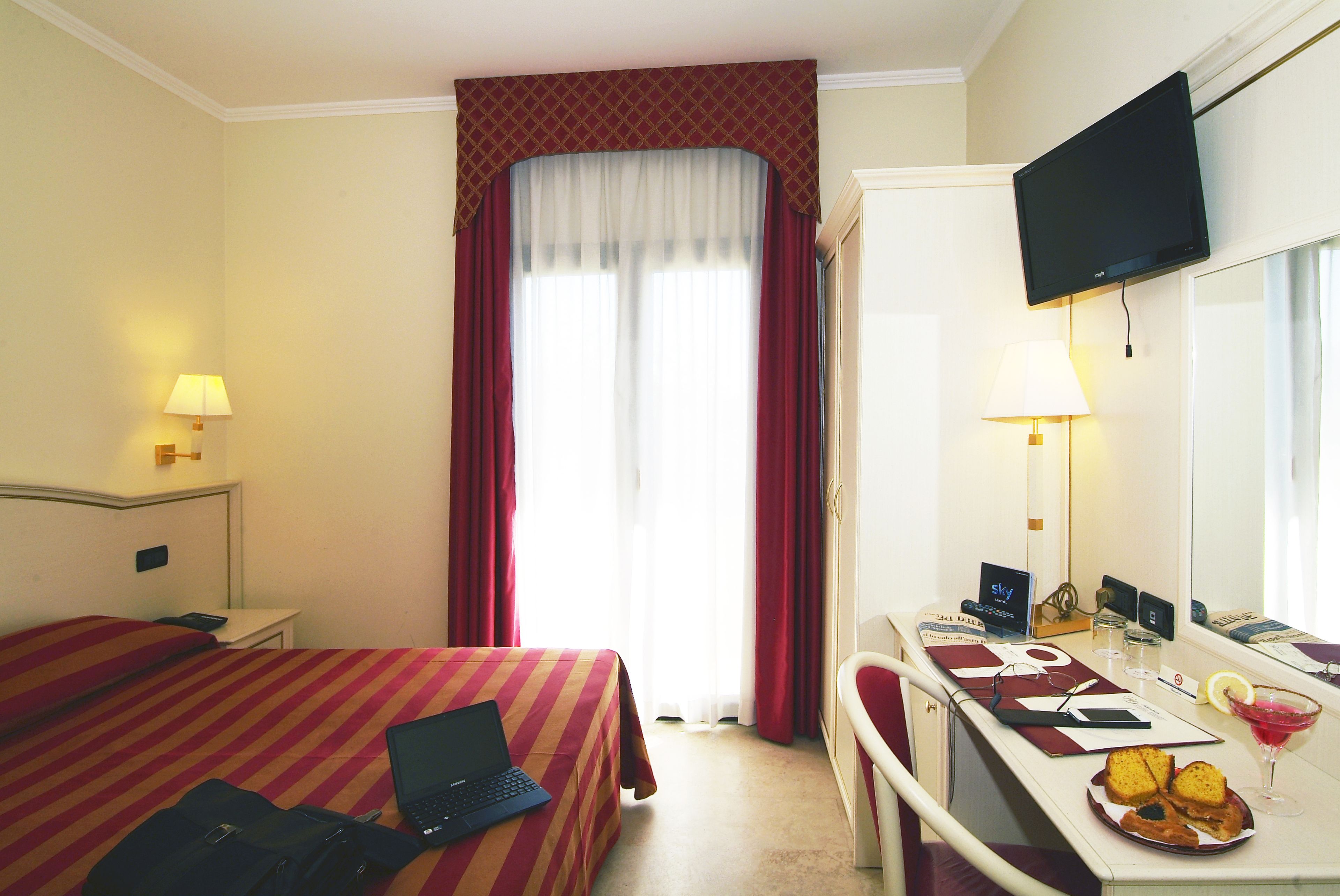 A hotel room with a bed, a desk with a laptop, a TV, and a breakfast tray.