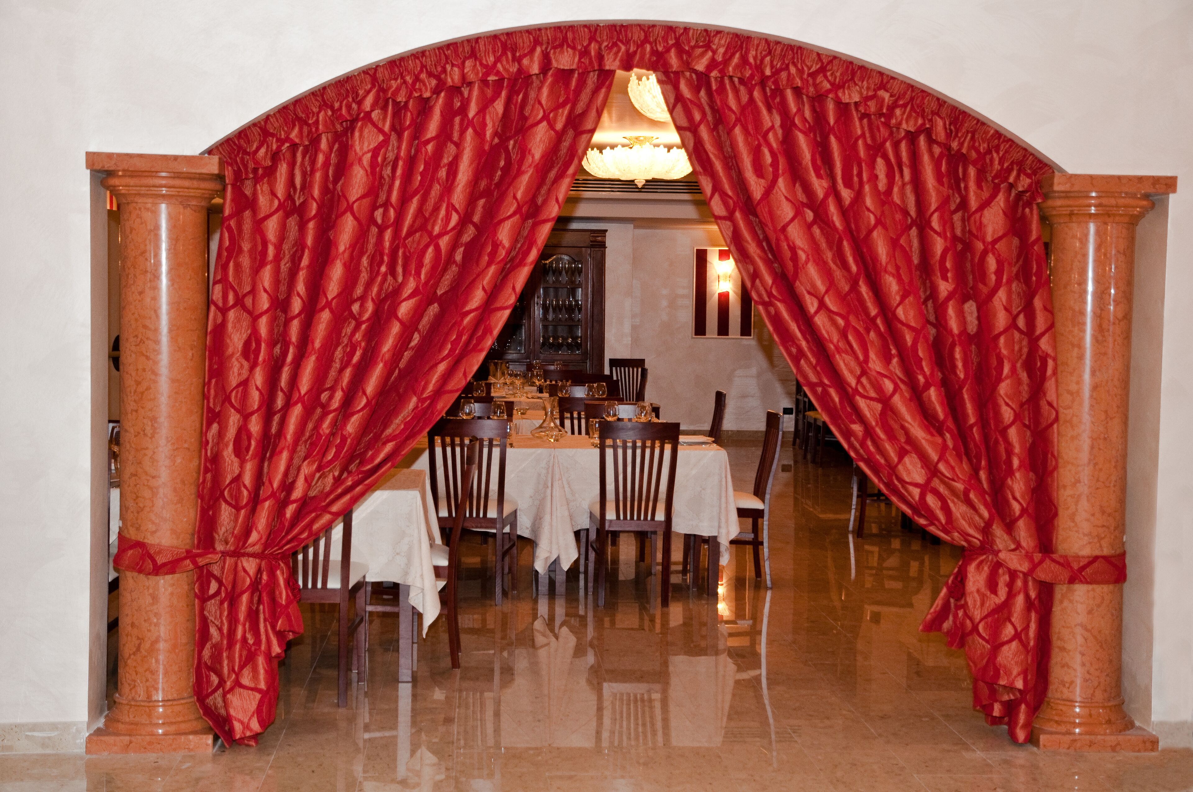 Un arco con tende rosse, una sala da pranzo con tavoli e sedie, e un lampadario.