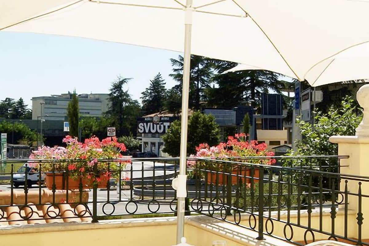 A table set with breakfast items, including croissants and a drink, under a large umbrella on an outdoor patio with a view of buildings and a sign that reads "SVUOT".
