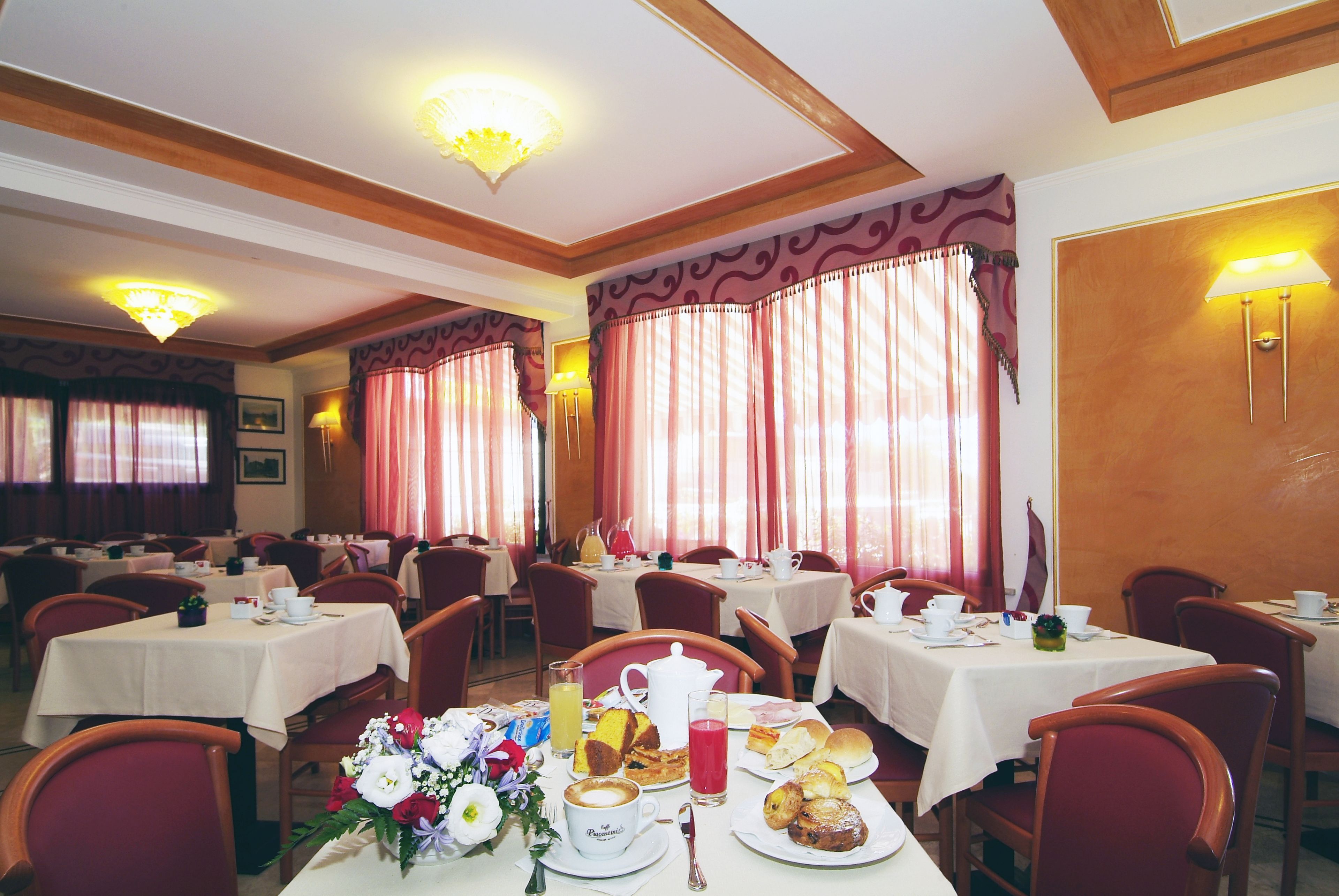 A dining area with tables set for breakfast, including pastries, coffee, and fruit.