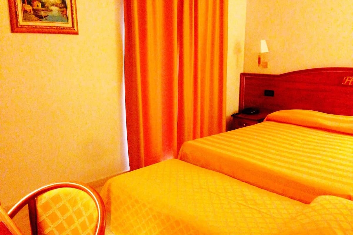 A hotel room with a bed, a chair, a nightstand, and a painting on the wall.