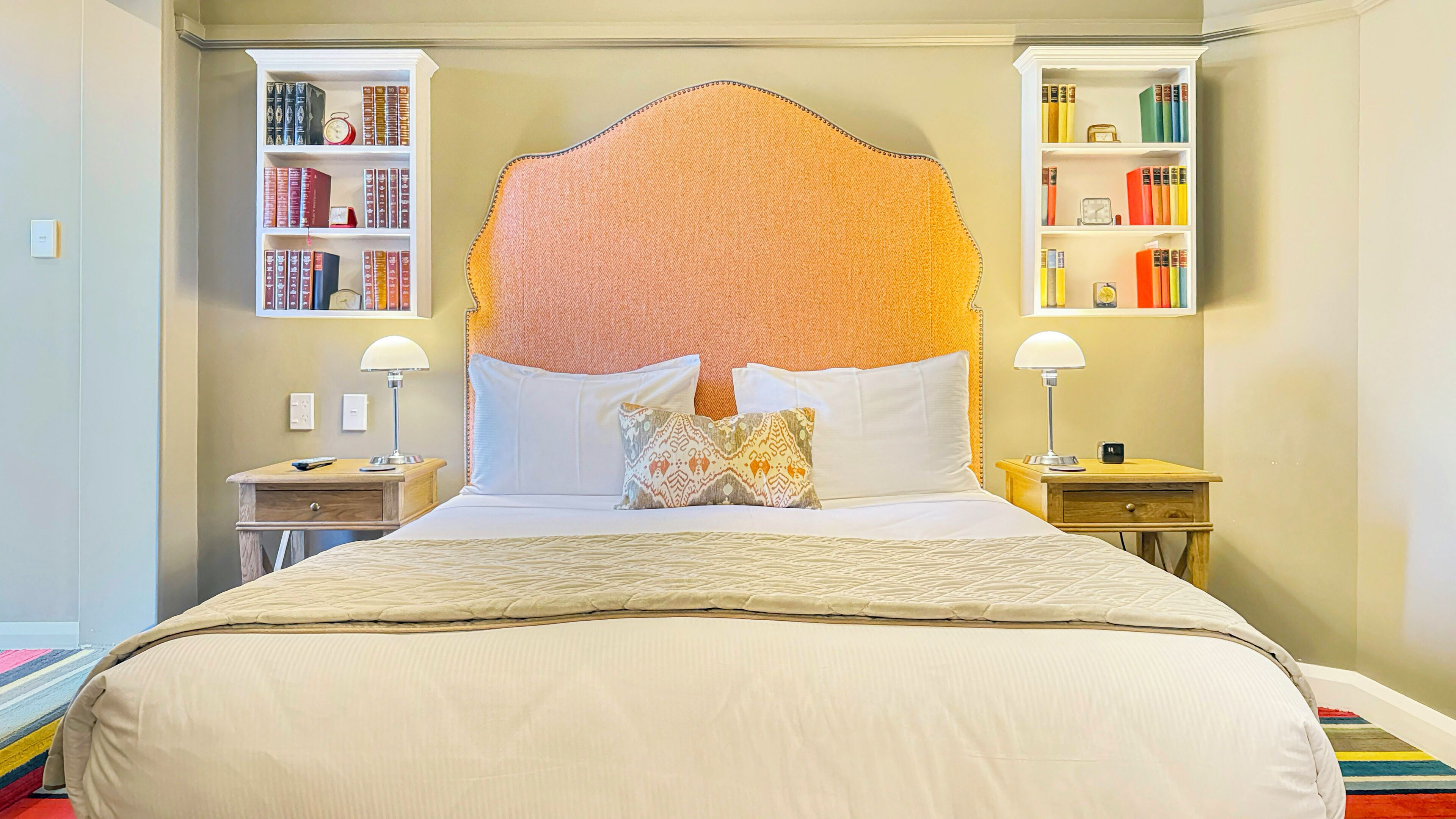 A hotel room with a large bed, two bedside tables with lamps, and built-in bookshelves on either side of the bed.