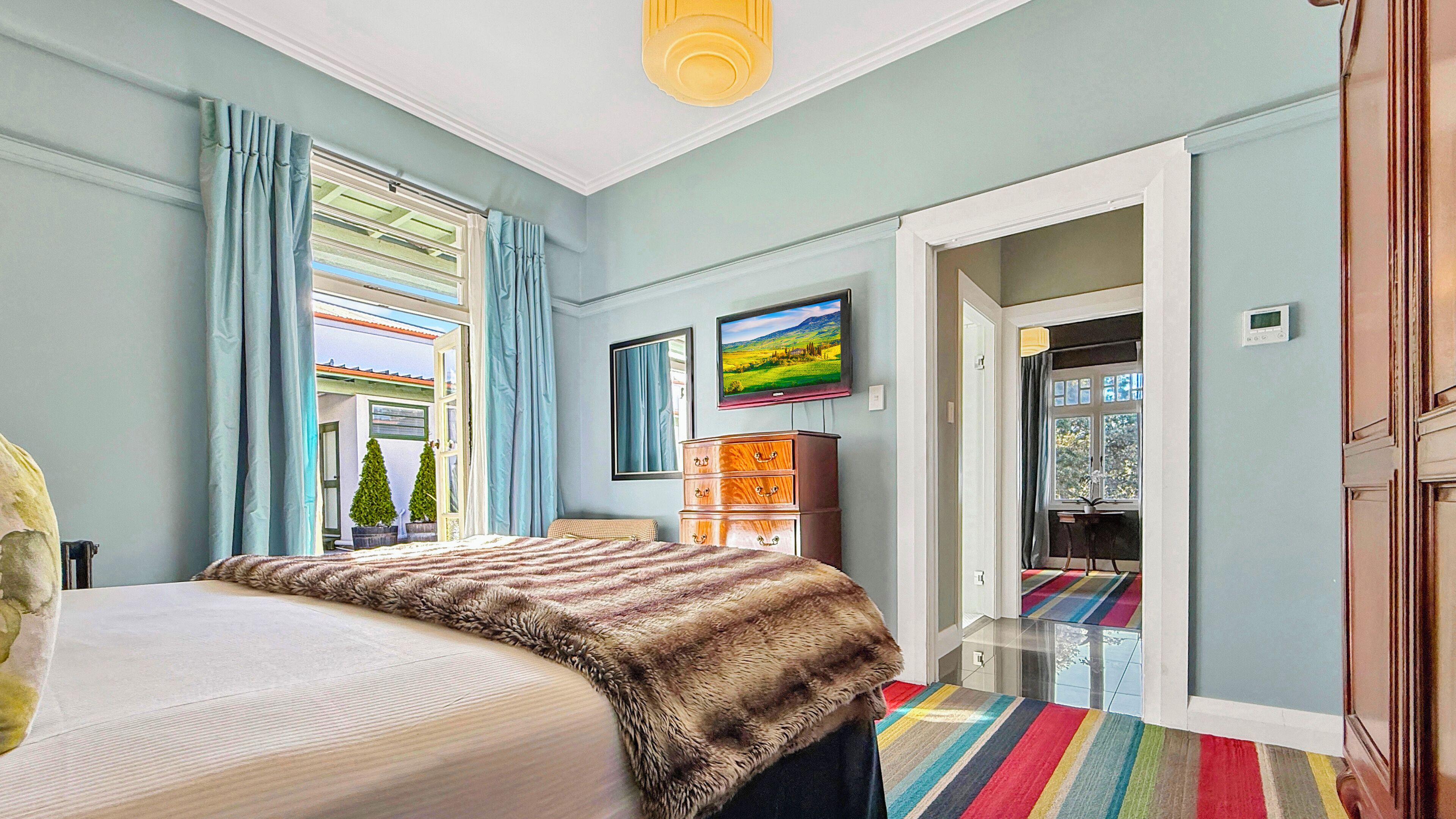 Une chambre à coucher avec un lit, une commode, un téléviseur et une fenêtre avec des rideaux.