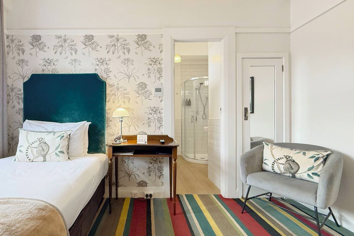 A hotel room with a bed, a desk, a chair, a shower area, and a door.