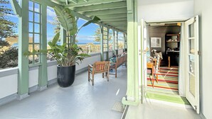 En inglasad veranda med en krukväxt, tränstolar och utsikt över havet.