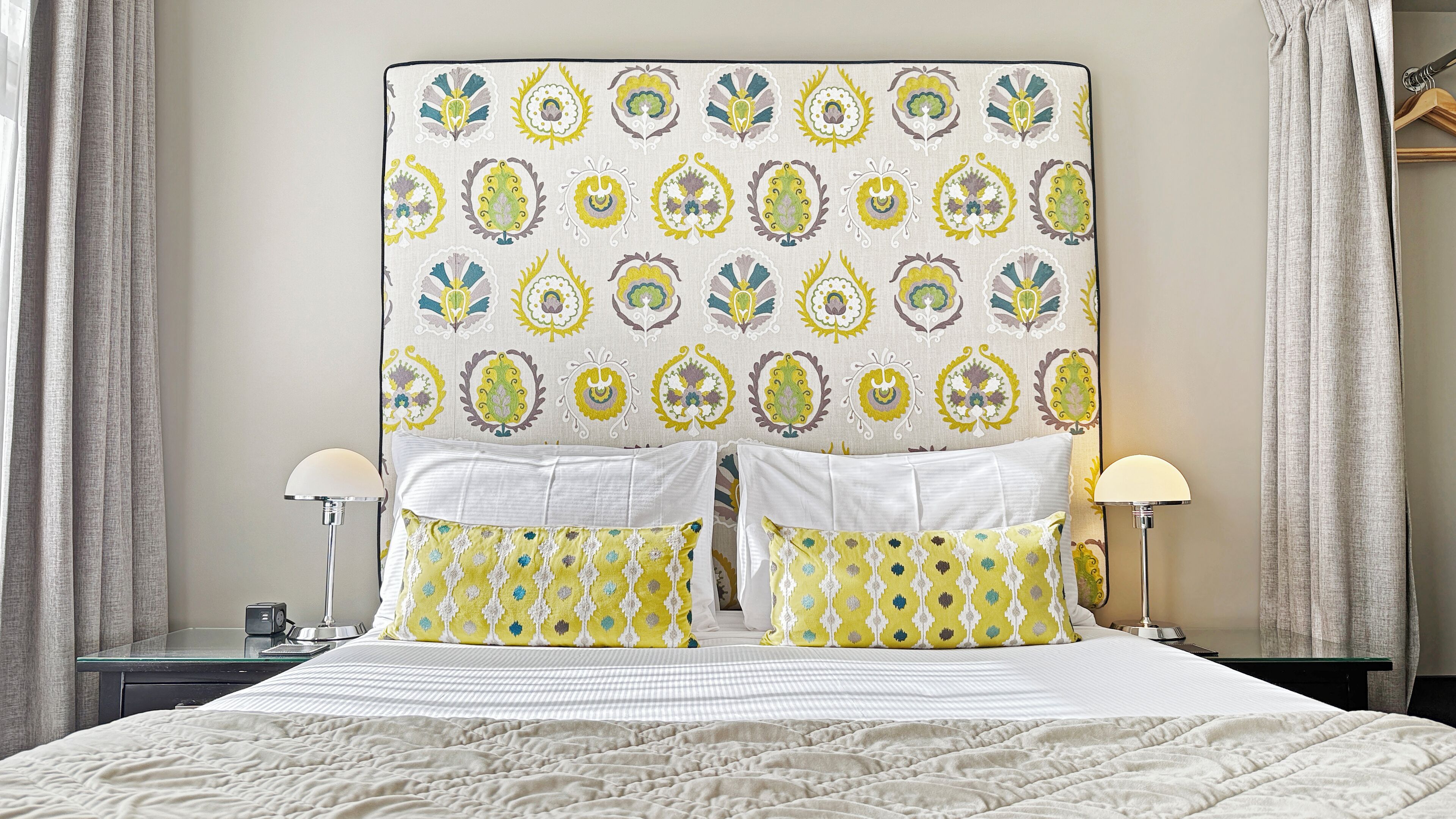 Una cama bien tendida con un cabecero estampado, dos lámparas de noche y una mesita de noche con lámpara.