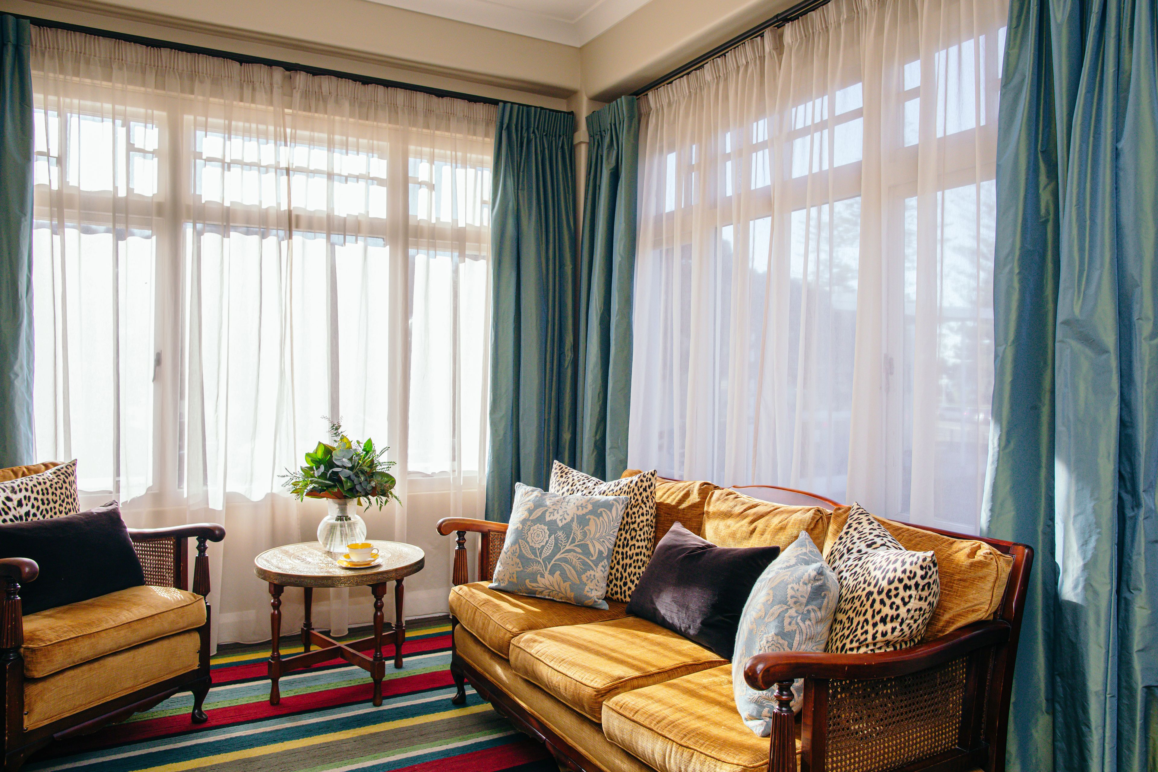 A living room with a sofa, armchairs, a small round table with a vase, and curtains.