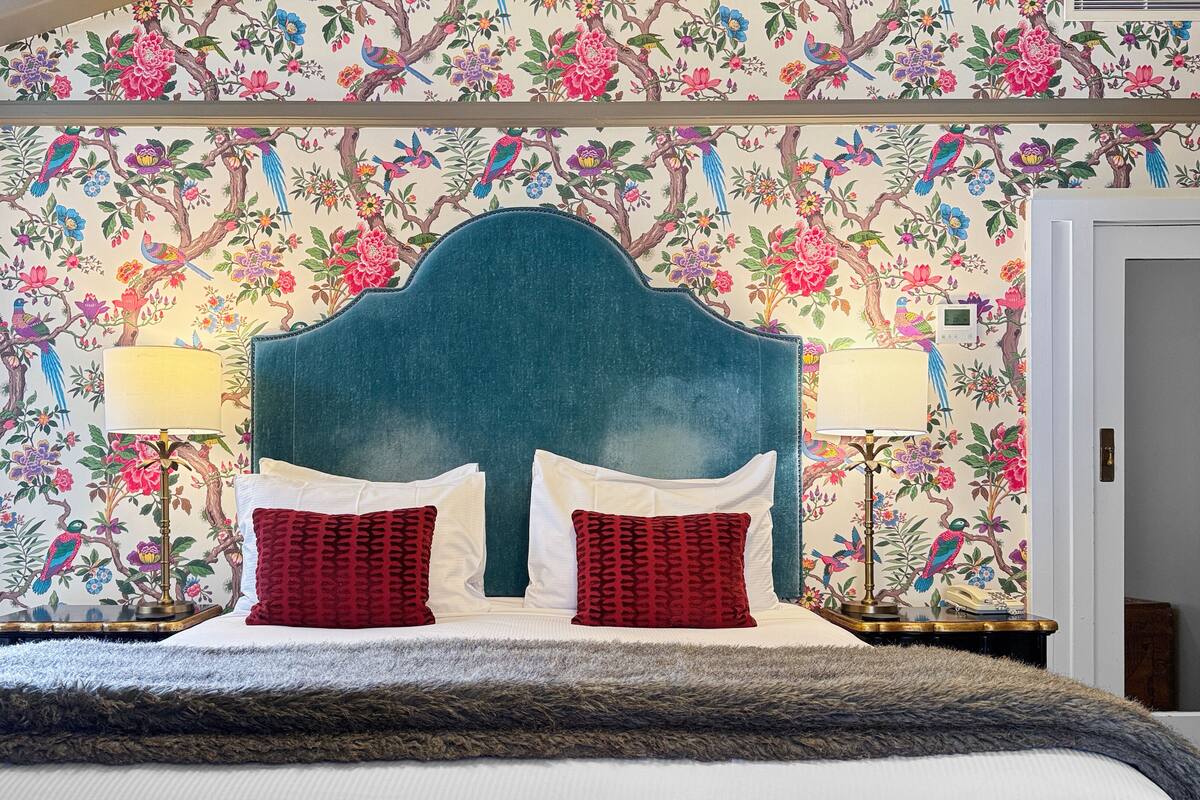 A bed with a blue headboard, two red pillows, and a fluffy grey blanket.
