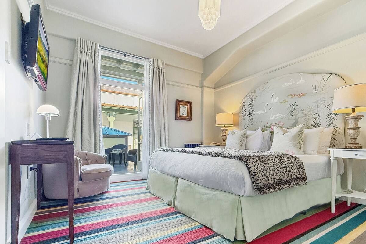 A hotel room with a large bed, two bedside lamps, a desk, a chair, and a colorful striped rug.