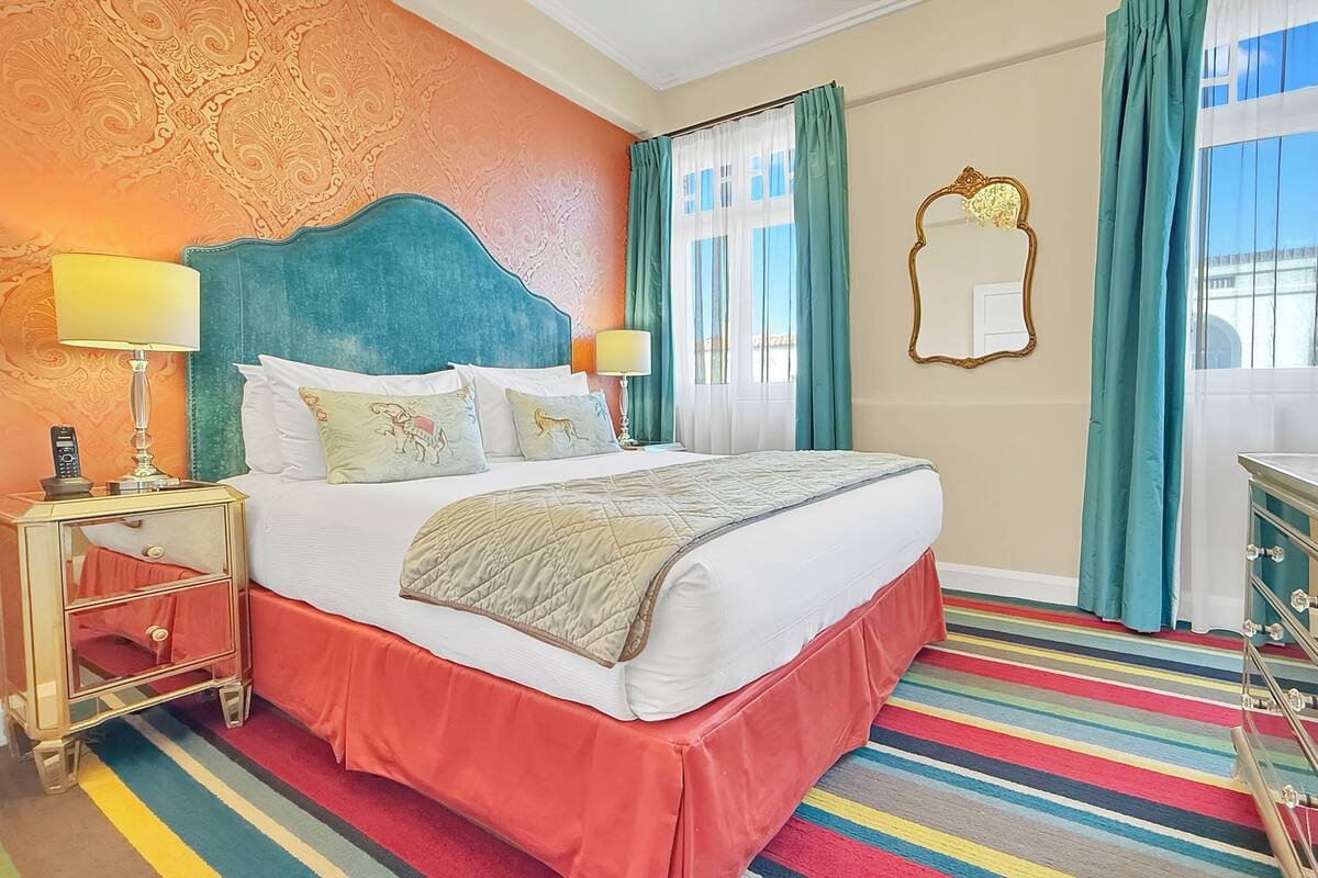 A hotel room with a large bed, a nightstand with a lamp, a dresser, and a mirror.