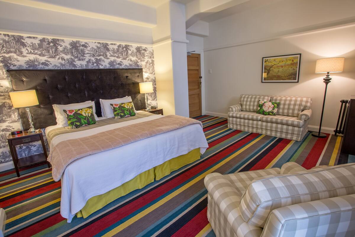 A hotel room with a large bed, a sofa, a chair, a lamp, and a painting on the wall.