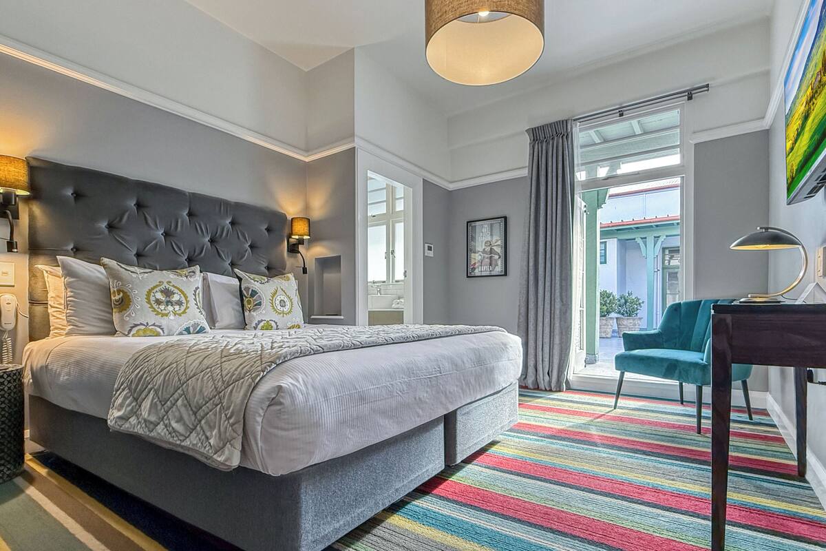 A modern hotel room with a large bed, a desk, and a view of the outside.