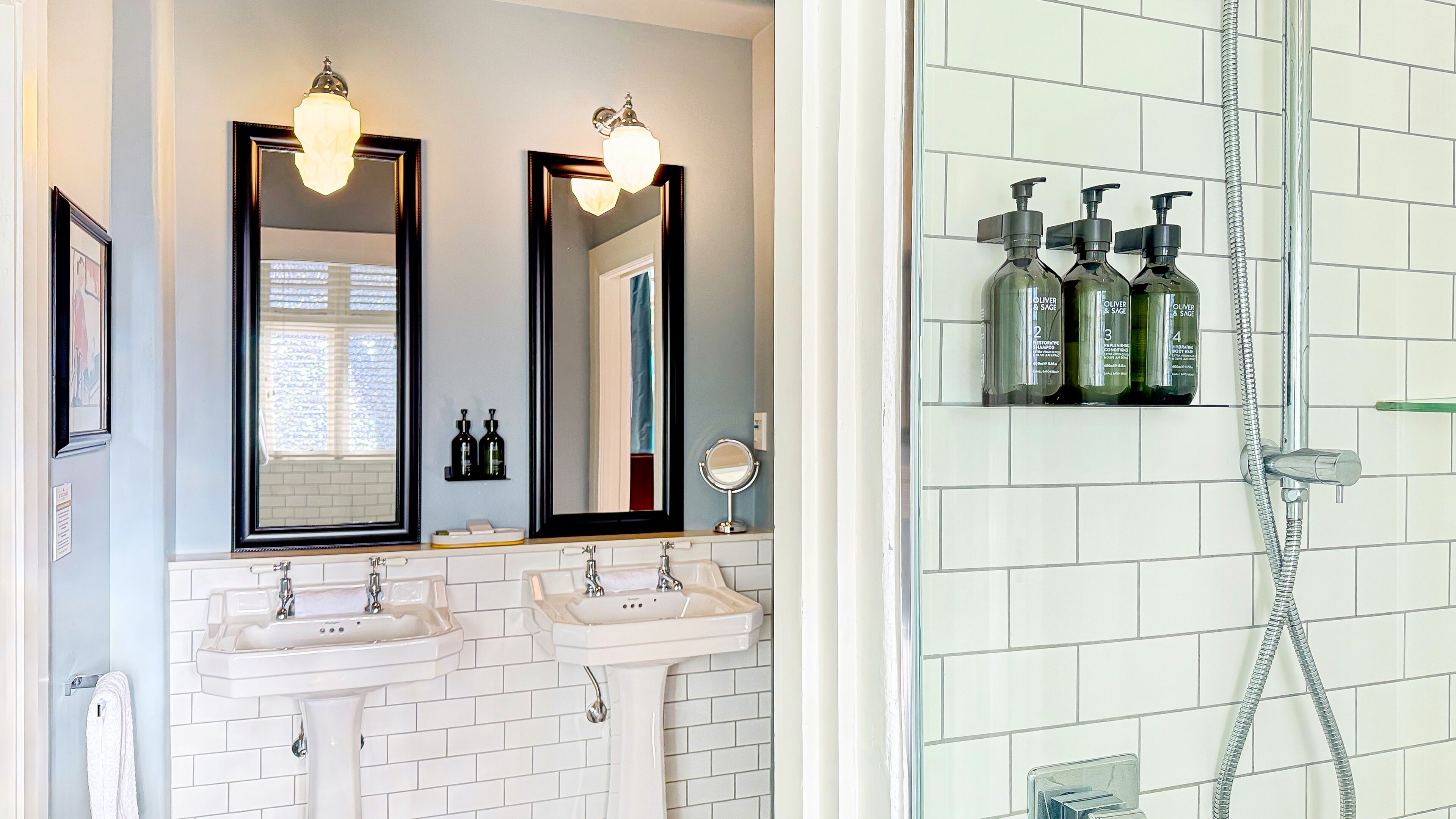 A bathroom with two sinks, a mirror, and a shower with a hose.
