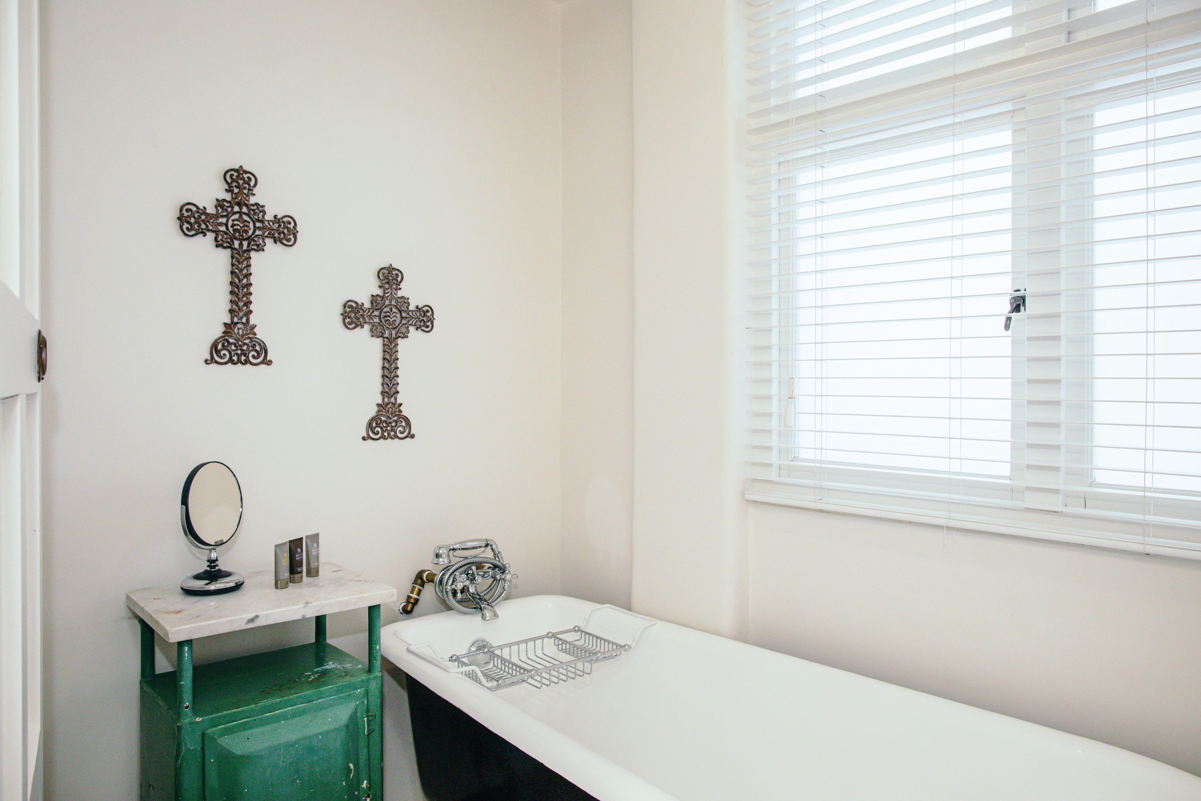 A bathroom with a white bathtub, a green cabinet, a mirror, and two decorative crosses on the wall.