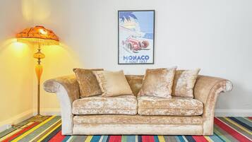 Un divano vintage con cuscini, una lampada da terra e un quadro di una macchina su un tappeto a righe.
