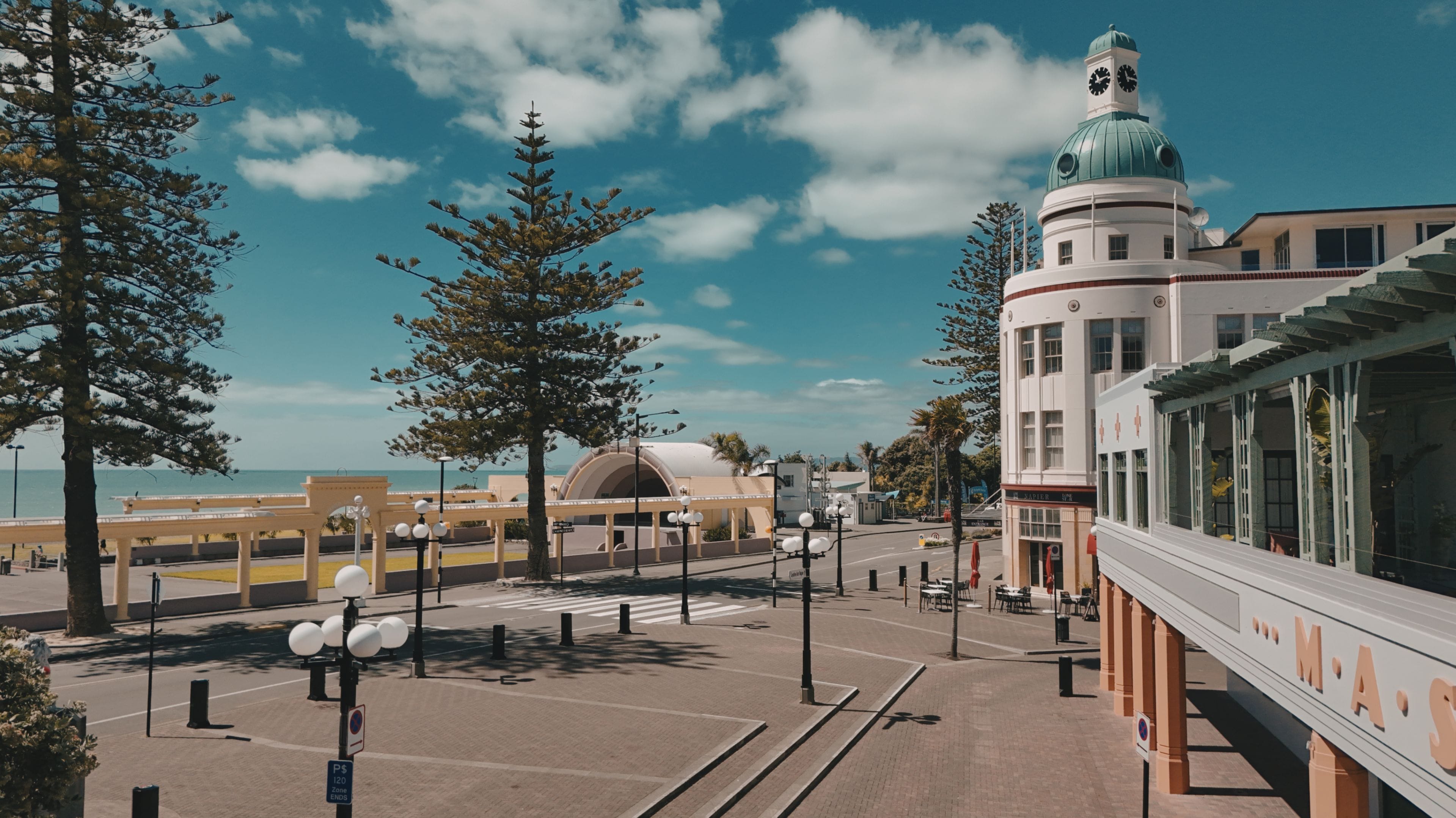 Vista de la calle con una línea de tranvía, un edificio con torre del reloj y una playa al fondo.