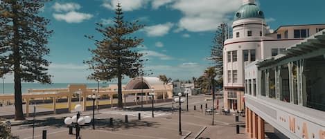 A street view with a tram line, a building with a clock tower, and a beach in the background.