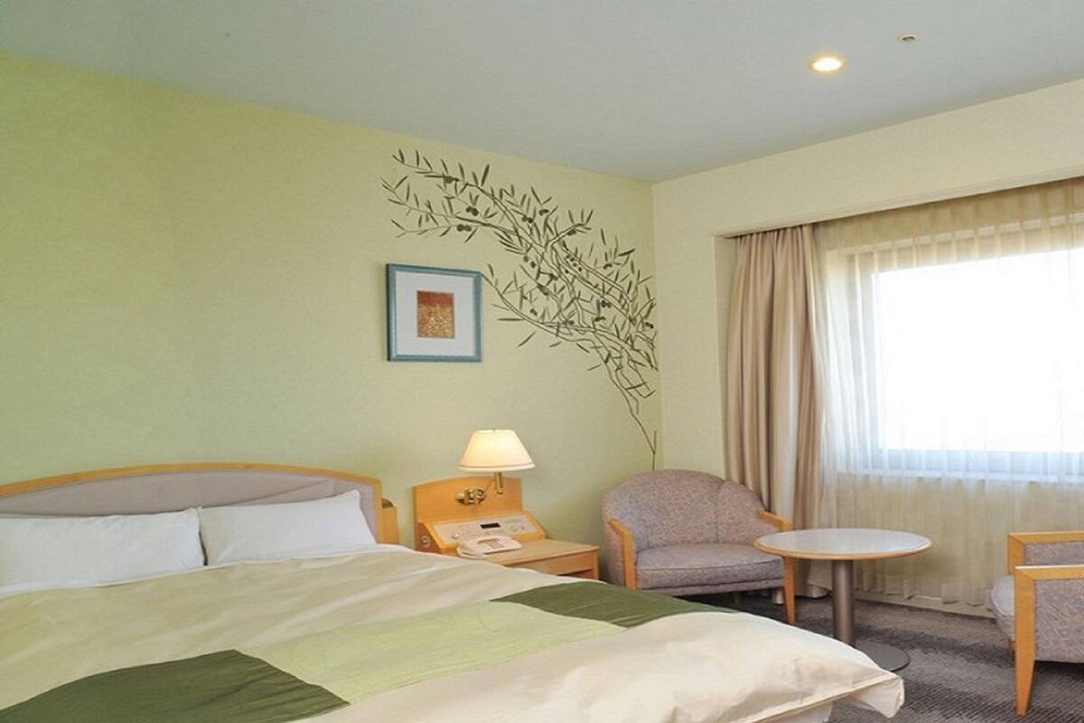 A hotel room with a bed, a chair, a small table, a lamp, and a window with curtains.